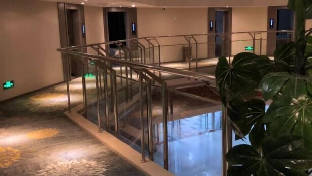 Un vestíbulo de hotel con barandilla de cristal, una fuente central y una planta grande.