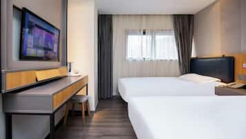 Habitación de hotel con dos camas, un escritorio, un televisor y una ventana con cortinas.