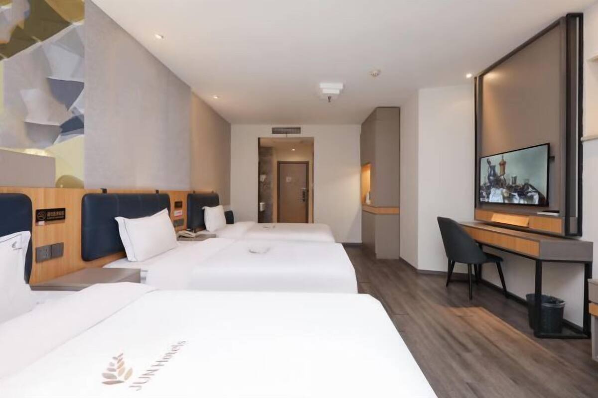 A hotel room with two beds, a desk, a chair, and a television.