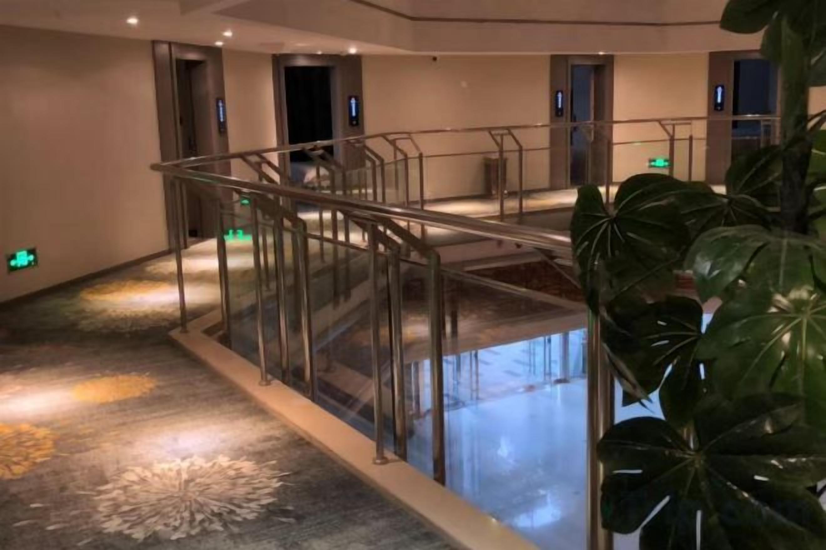 A hotel lobby with a glass railing, a water feature, and a large plant.