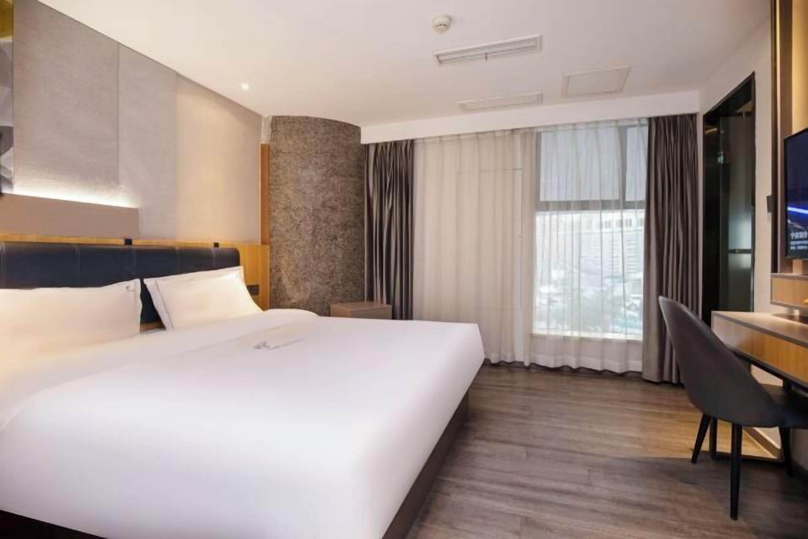A hotel room with a large bed, a desk, a chair, a television, and a window with curtains.
