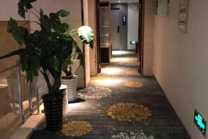 Un couloir avec un tapis orné d’un motif floral, des plantes en pot et une main courante sur le côté gauche.