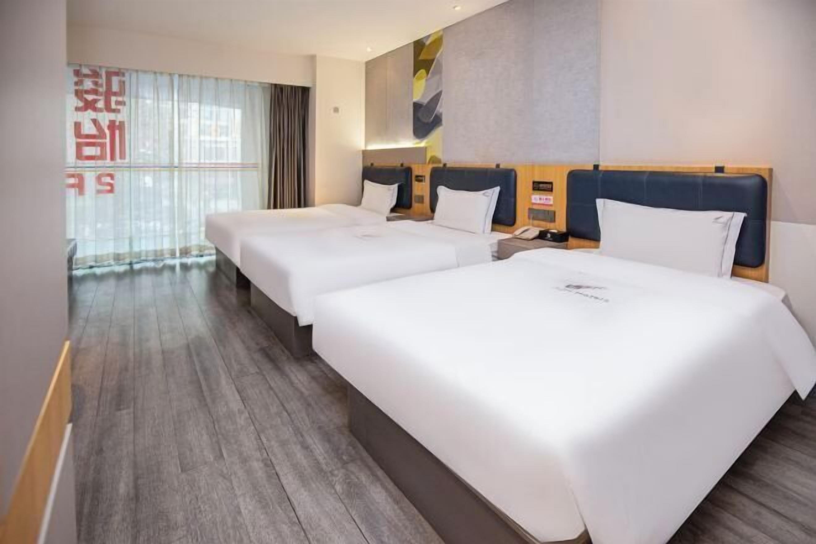 Une chambre d’hôtel avec deux lits, un plancher en bois, une grande fenêtre avec des rideaux et un décor mural moderne.