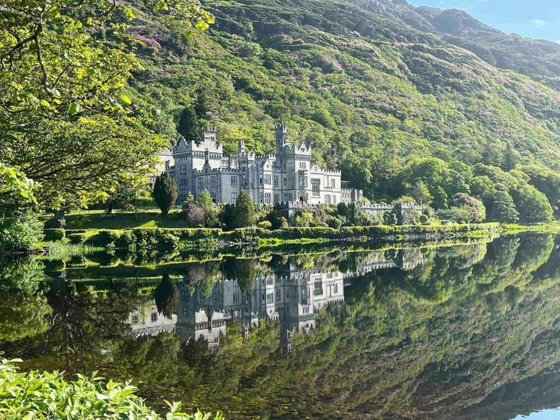 A castle with a large body of water in front, surrounded by lush greenery and hills.