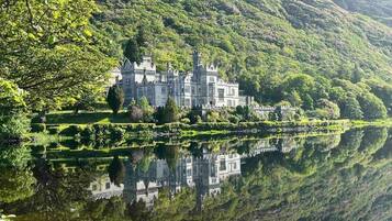 A castle with a large body of water in front, surrounded by lush greenery and hills.