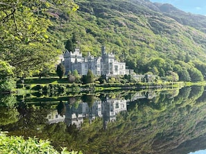 A castle with a large body of water in front, surrounded by lush greenery and hills. - Lakeside Apartment Retreat in Oughterard Connemara (Oughterard)