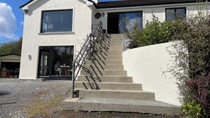 A two-story house with a concrete staircase, a garage, and a patio area with outdoor seating. - Lakeside Apartment Retreat in Oughterard Connemara (Oughterard)