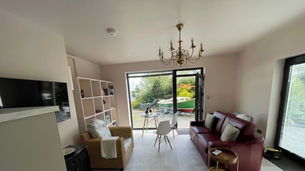 A living room with a red sofa, a wicker chair, a bookshelf, and a television. - Lakeside Apartment Retreat in Oughterard Connemara (Oughterard)