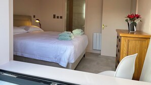 A hotel room with a neatly made bed, a bedside lamp, a radiator, and a wooden cabinet with a vase of flowers. - Lakeside Apartment Retreat in Oughterard Connemara (Oughterard)