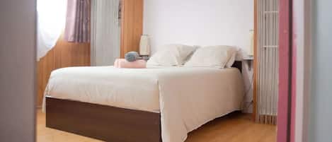 A modern bedroom with a wooden floor, a bed with white bedding, and a bedside table with a lamp.