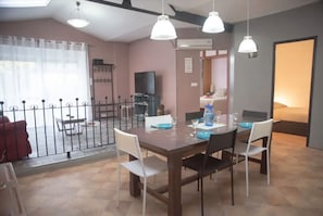 A dining area with a wooden table, white chairs, and pendant lights. There is a television and a bed in the background. - Carpentry - 2 bedrooms - air conditioning - wifi (Châteauroux)