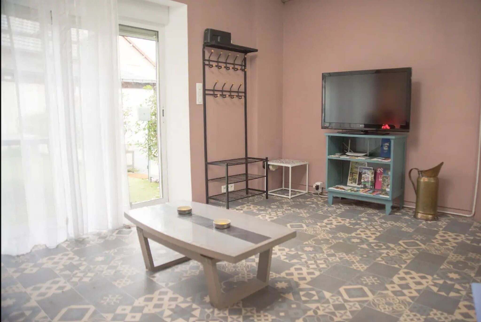 A room with a table, a TV on a stand, a coat rack, and a bookshelf.