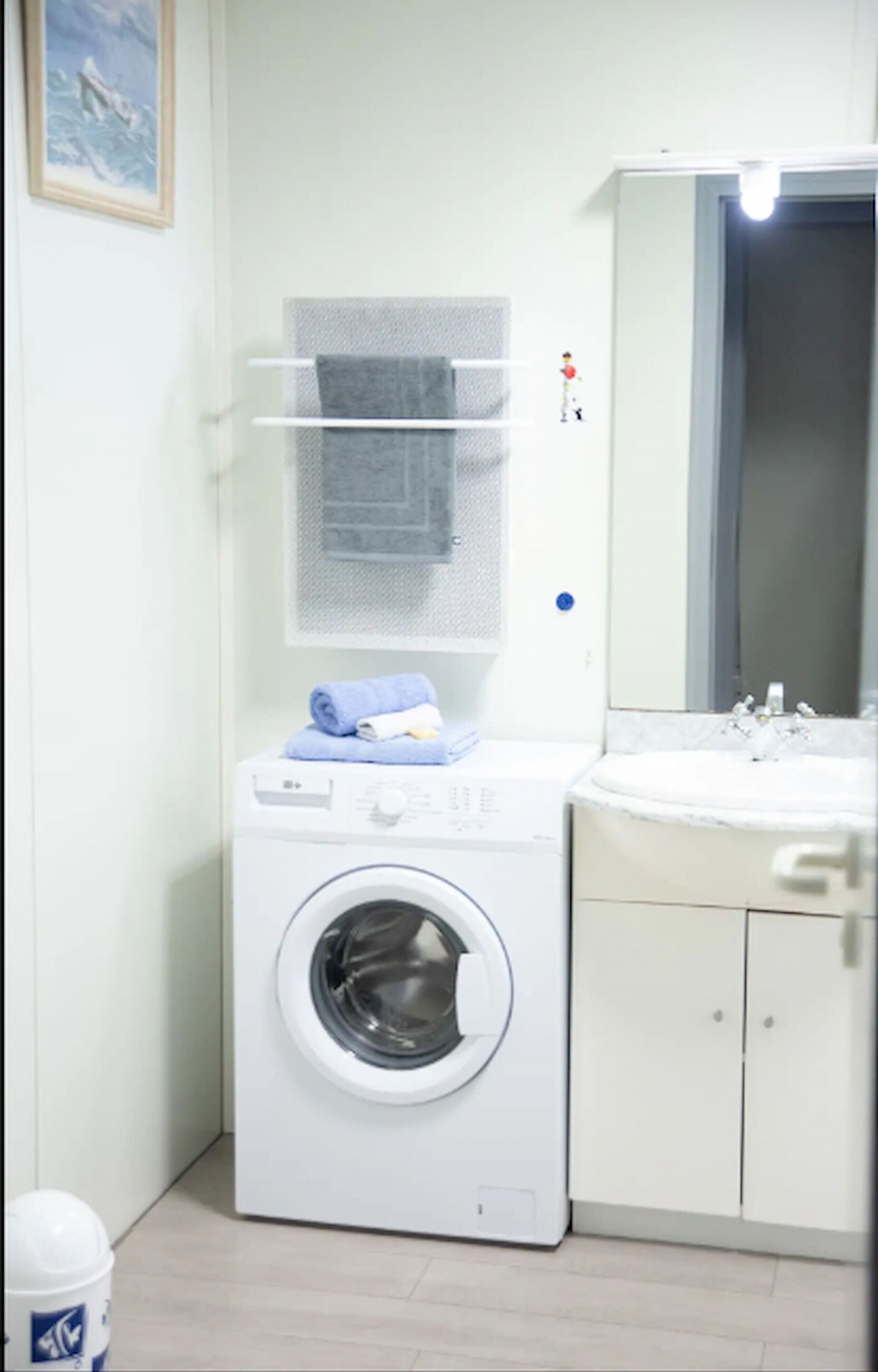 Une petite buanderie équipée d’un lave-linge à chargement frontal, d’un étendoir et d’un évier.