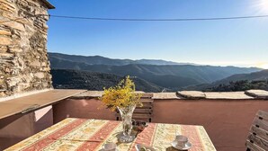 A table set with a vase of yellow flowers, a plate of food, and a cup on a table with a striped tablecloth, overlooking a mountainous landscape.