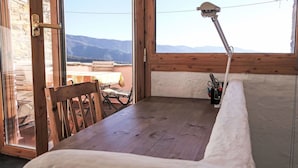 A wooden bench with a white cushion, a table with a tablecloth, and a window with a view of mountains. - Stunning  villa for 4 people with WIFI, terrace and panoramic view (Prelà Castello)