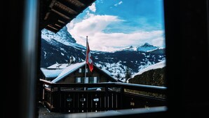 Un chalet doté d’un toit en bois et d’un drapeau rouge, offrant une vue sur des montagnes enneigées et un ciel dégagé.