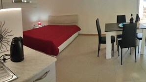 Habitación pequeña con cama, una mesa de comedor con sillas, un hervidor y un mueble bajo.