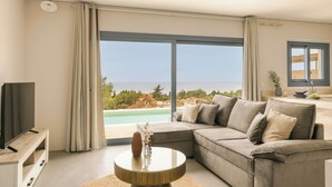 A modern living room with a large window, a sofa, a coffee table, and a TV. - Villa Ivi - Zen Villas (Fiskardo)