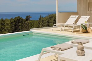 Piscina com espreguiçadeiras e toalhas brancas, um vaso e vista para o oceano.