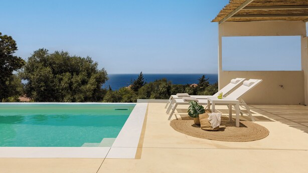 A poolside area with a view of the sea, white lounge chairs, and a covered seating area. - Villa Ivi - Zen Villas (Fiskardo)