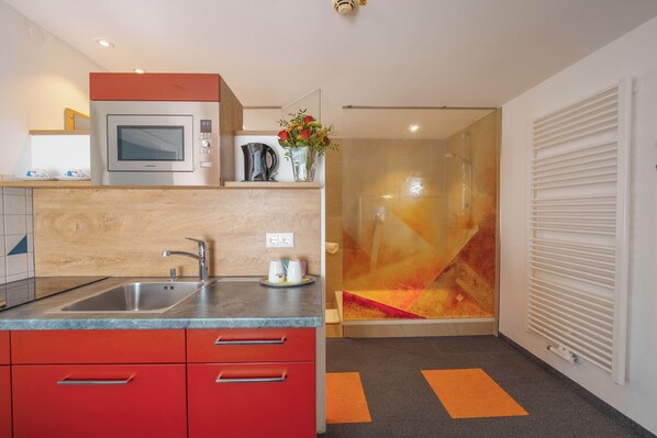 A modern kitchen with a built-in microwave, a sink, and red cabinets. - Altötting City Apartments (Altötting)