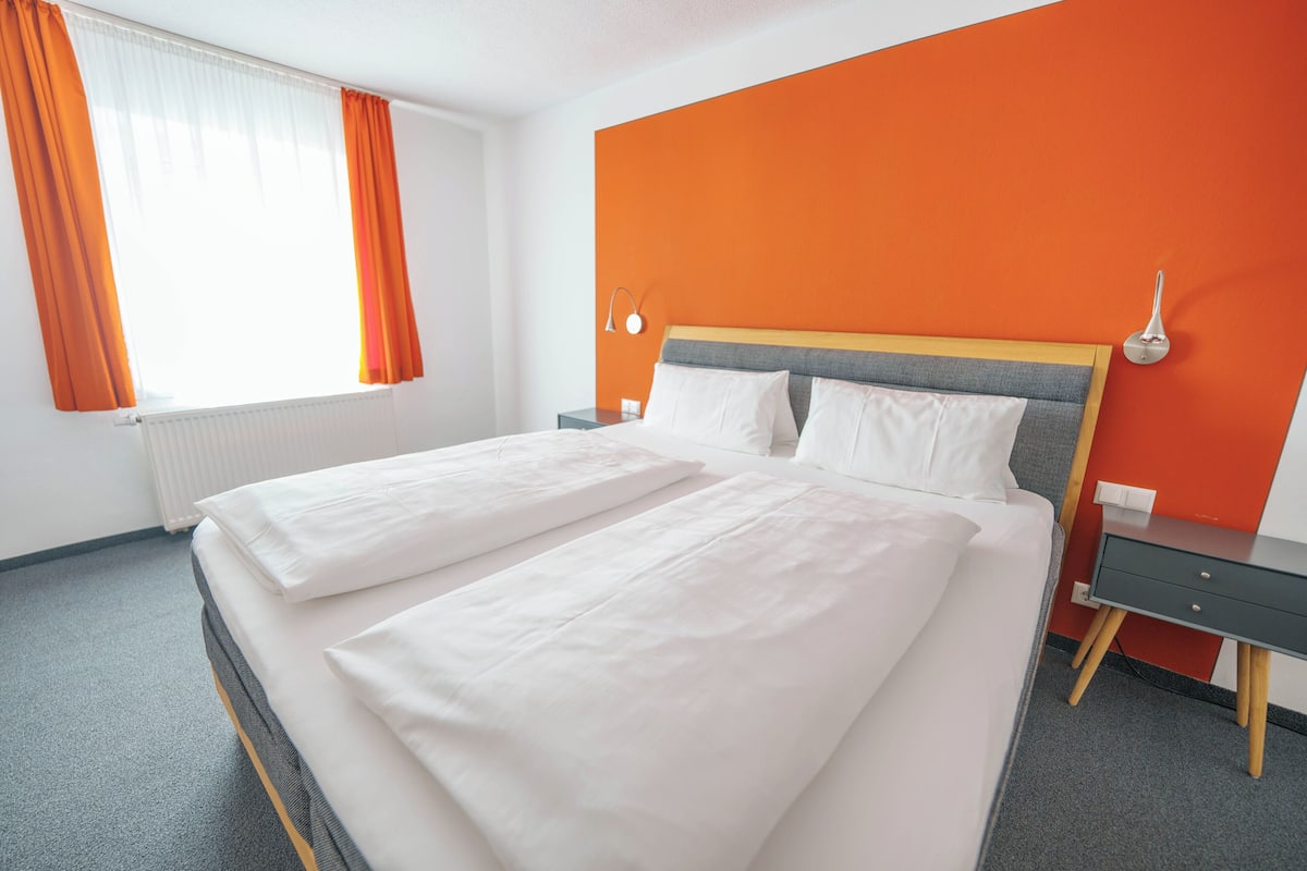 A hotel room with a bed, a nightstand, a lamp, and a window with curtains.