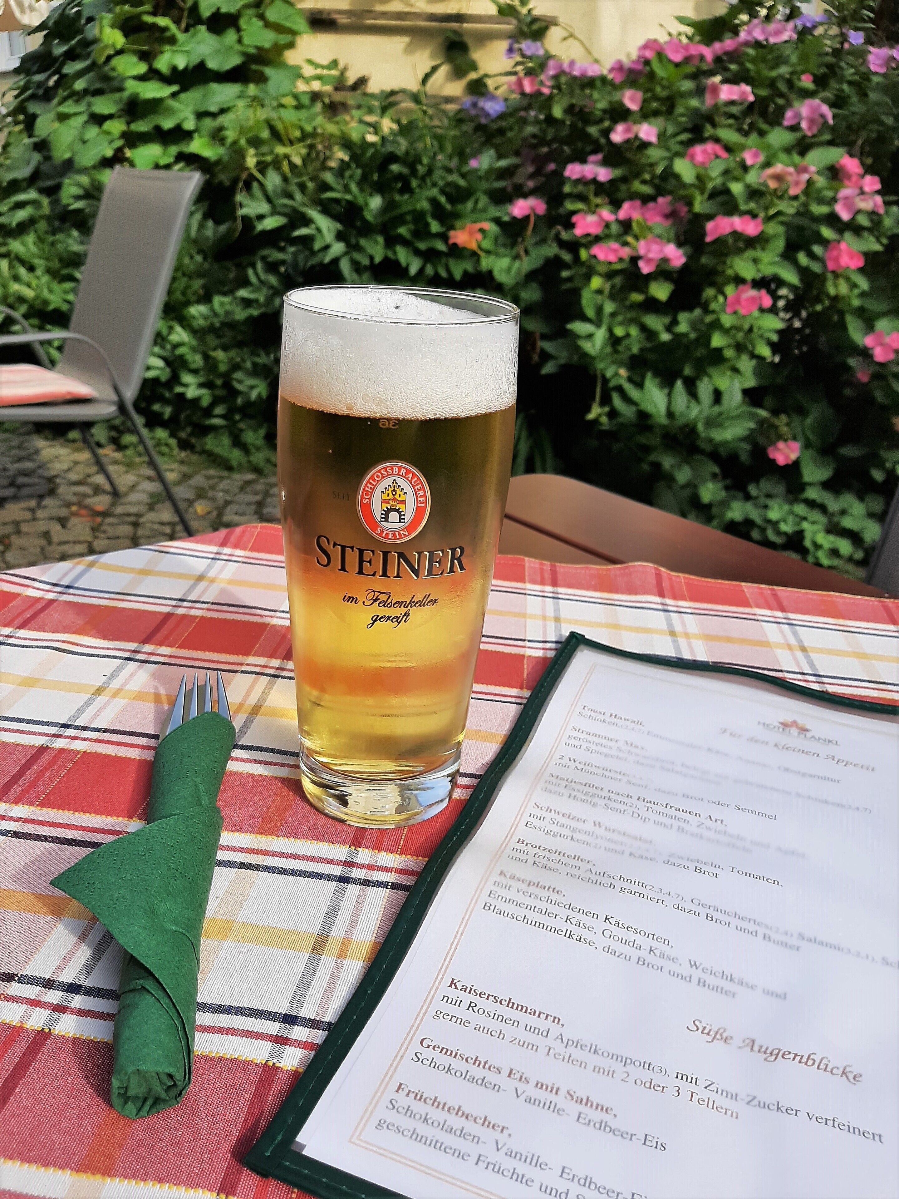 Una cerveza en una mesa con un menú y una servilleta doblada.