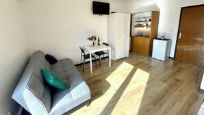 Un salon moderne avec un canap é gris, une table à manger avec des chaises, un coin cuisine doté de meubles en bois et un téléviseur à écran plat fixé au mur.