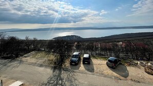 Un espace de stationnement avec trois voitures, une vue sur un lac et, au loin, une côte bordée de bâtiments.