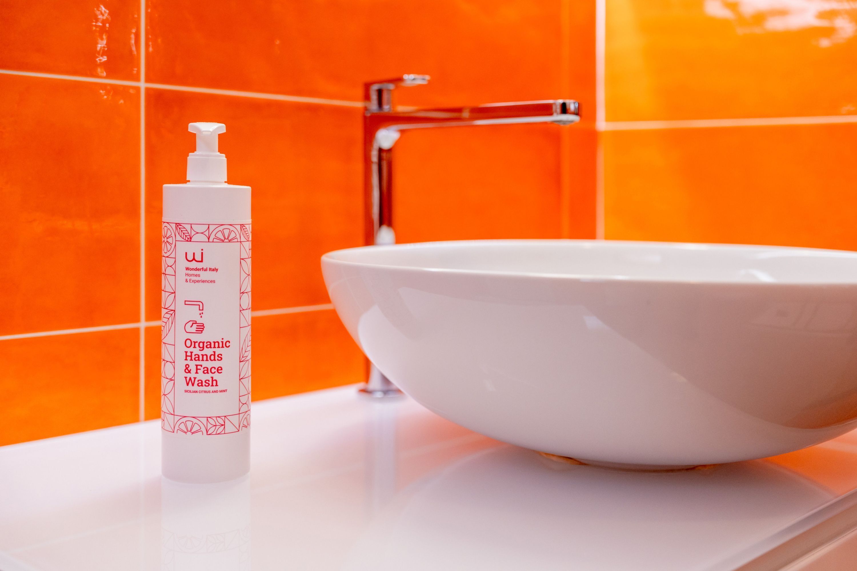 A bathroom with a white sink and an orange tiled wall.