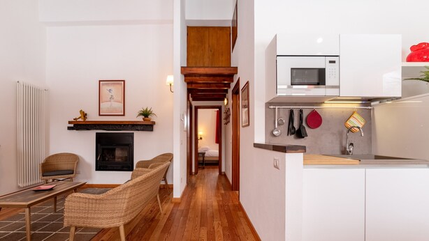 A modern living room with a fireplace, a dining area with wicker furniture, and a kitchen with white cabinets and a microwave. - Alma e Basili by Wonderful Italy (Bellagio)