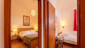 A hotel room with two beds, wooden flooring, a small table with a lamp, and a hanging light fixture. - Alma e Basili by Wonderful Italy (Bellagio)