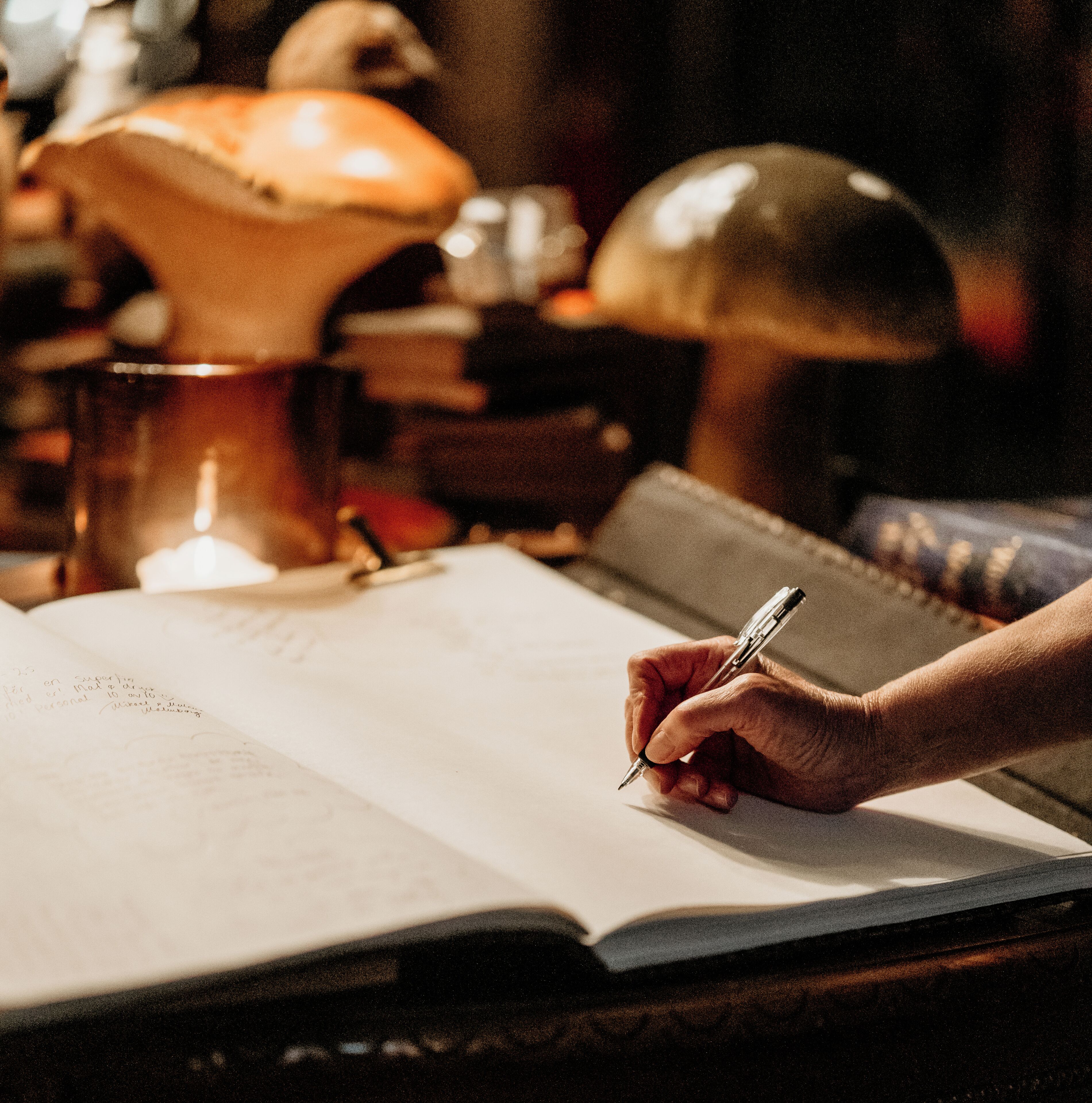 Een hand die met een pen in een notitieboek schrijft, een lamp en een onscherpe achtergrond.