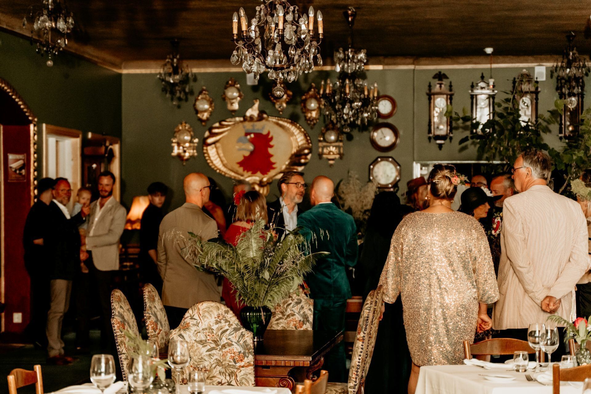 Un evento interior concurrido, con candelabros ornamentados, relojes antiguos y arreglos florales.