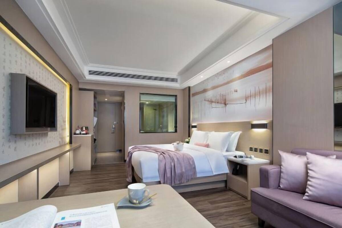 Moderni hotellihuone, jossa on sänky, yöpöytä ja oleskelualue, jossa on sohva.