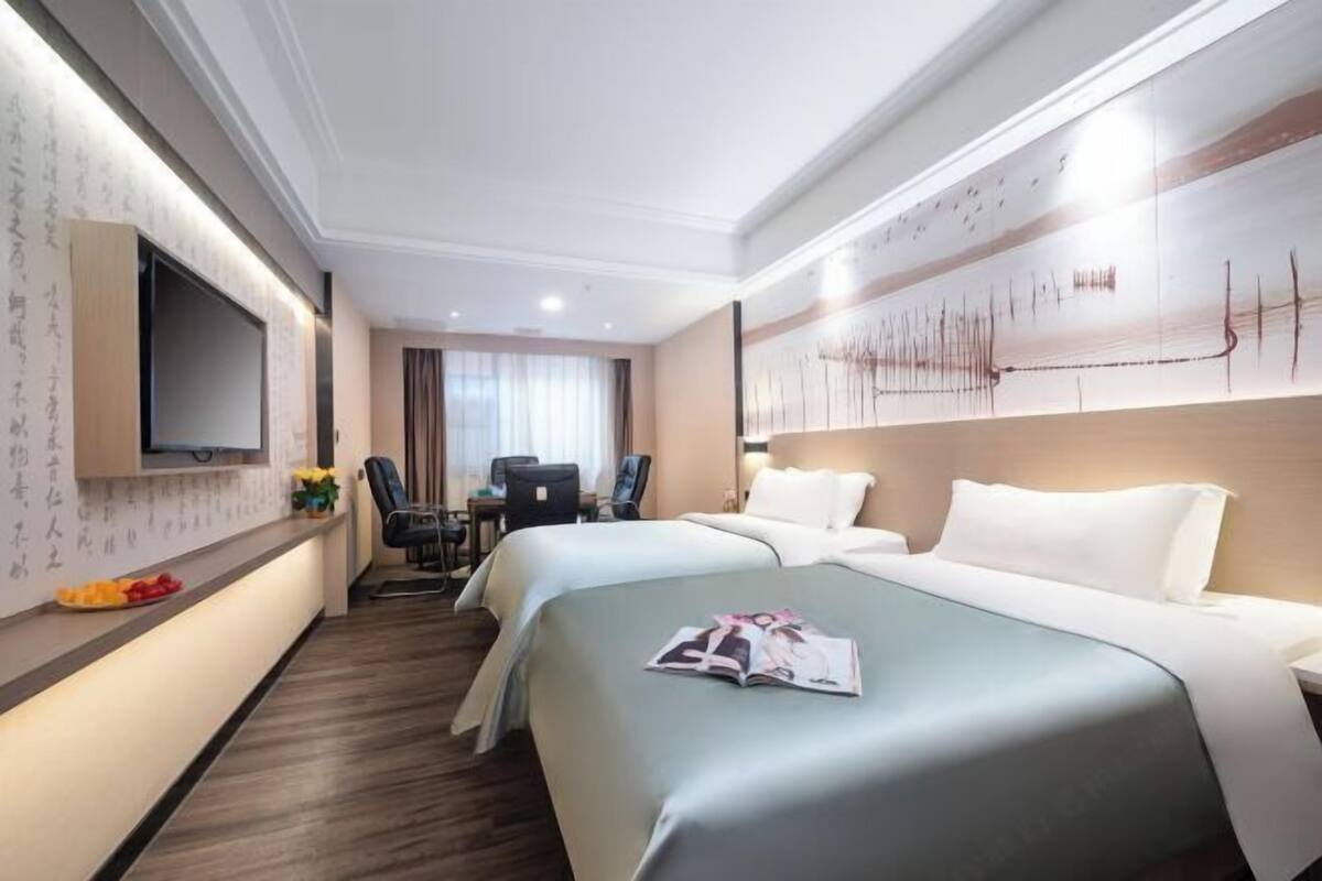Hotellihuone, jossa on kaksi sänkyä, työp öytä, tuoli, taulutelevisio ja seinä, jossa on nuotteja.
