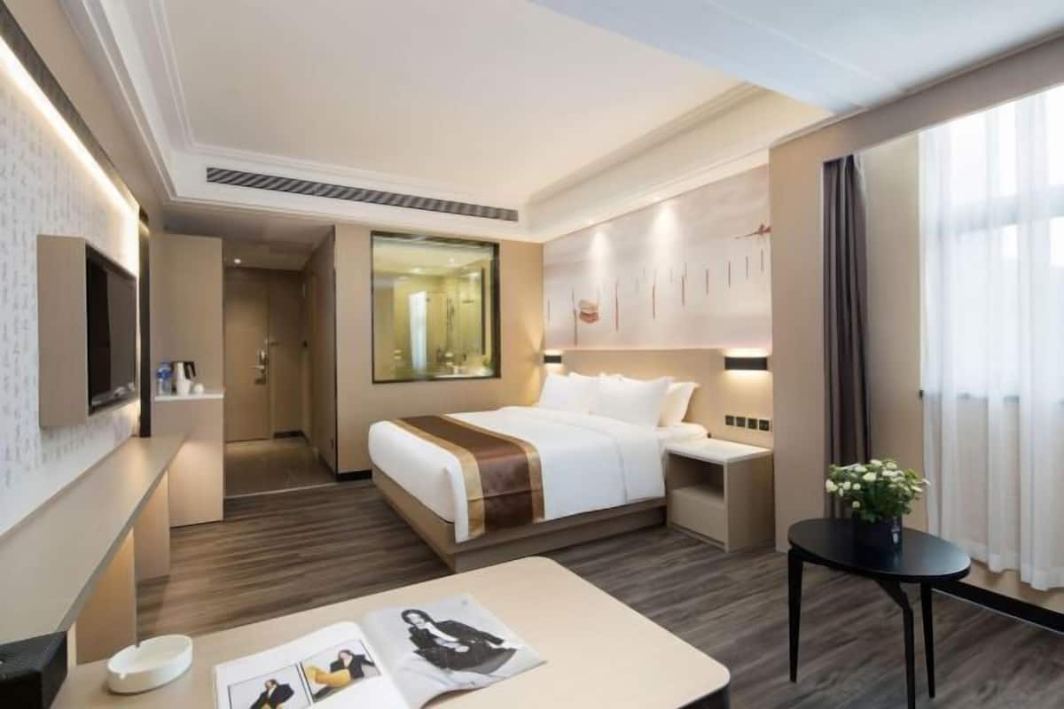 Hotellihuone, jossa on sänky, yöpöytä ja pieni pöytä, jonka päällä on kasvi.