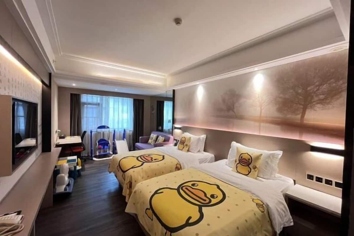 Hotellihuone, jossa on kaksi sänkyä, ja molemmissa on ankkoja kuvaava vuodevaatteisto. Lisäksi huoneessa on työpöytä tuolilla, televisio ja suuri ikkuna, jossa on verhot.