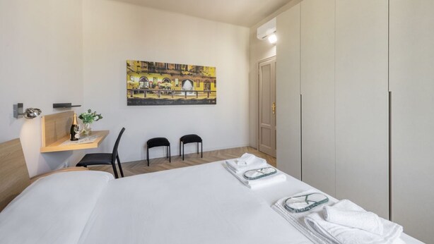 Una habitación de hotel con una cama, un escritorio con una silla, un cuadro en la pared y un armario.