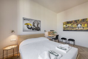 Una habitación de hotel con una cama, un escritorio, dos sillas y obras de arte en las paredes.