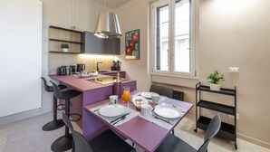 Una cocina compacta con comedor, máquina de café y una pequeña planta en un estante.