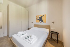 Une chambre d’hôtel avec un lit, des serviettes blanches, une petite table de chevet, une œuvre d’art murale et une porte.