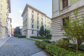 A cobblestone street flanked by multi-story buildings with balconies and a small garden area.