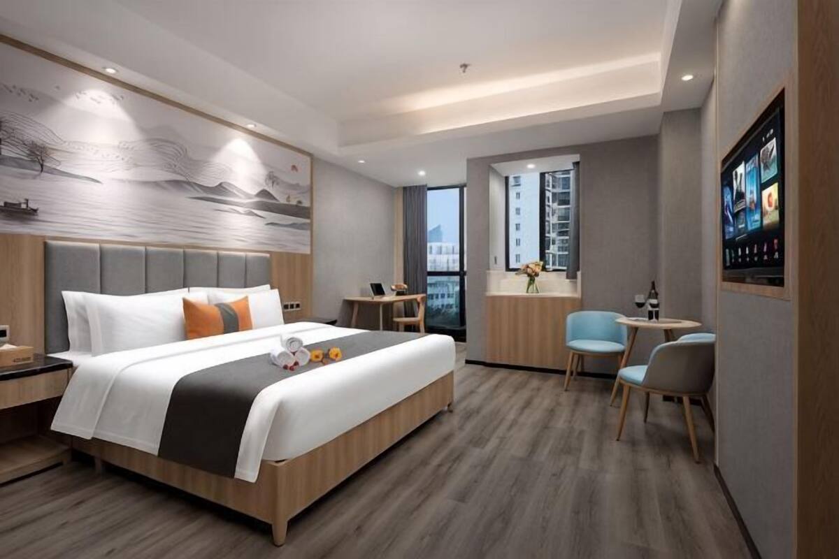 A modern hotel room with a large bed, a desk, and a view of the city.
