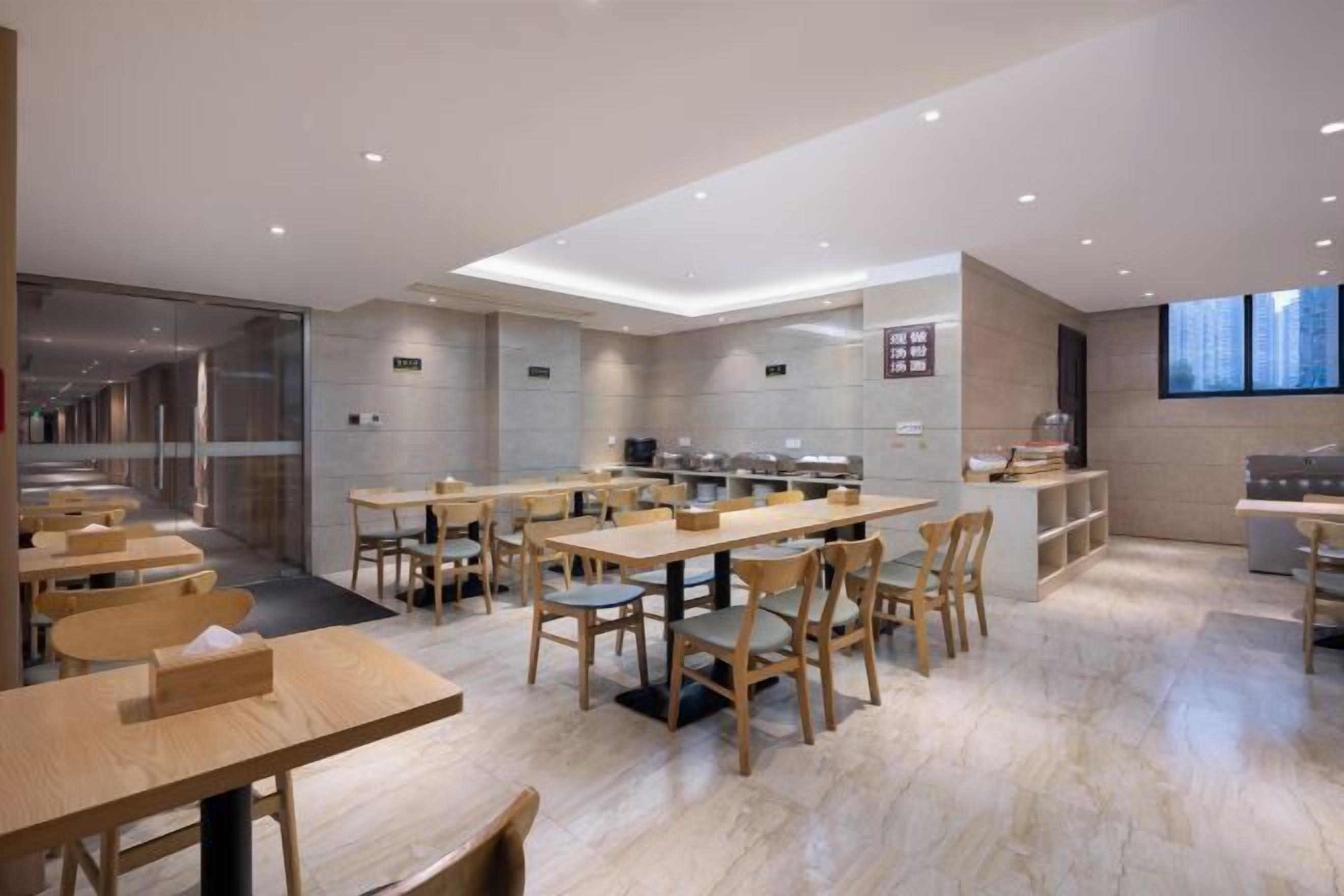 Een modern restaurant met houten tafels en stoelen, een keuken en een uitzicht op de stad door grote ramen.
