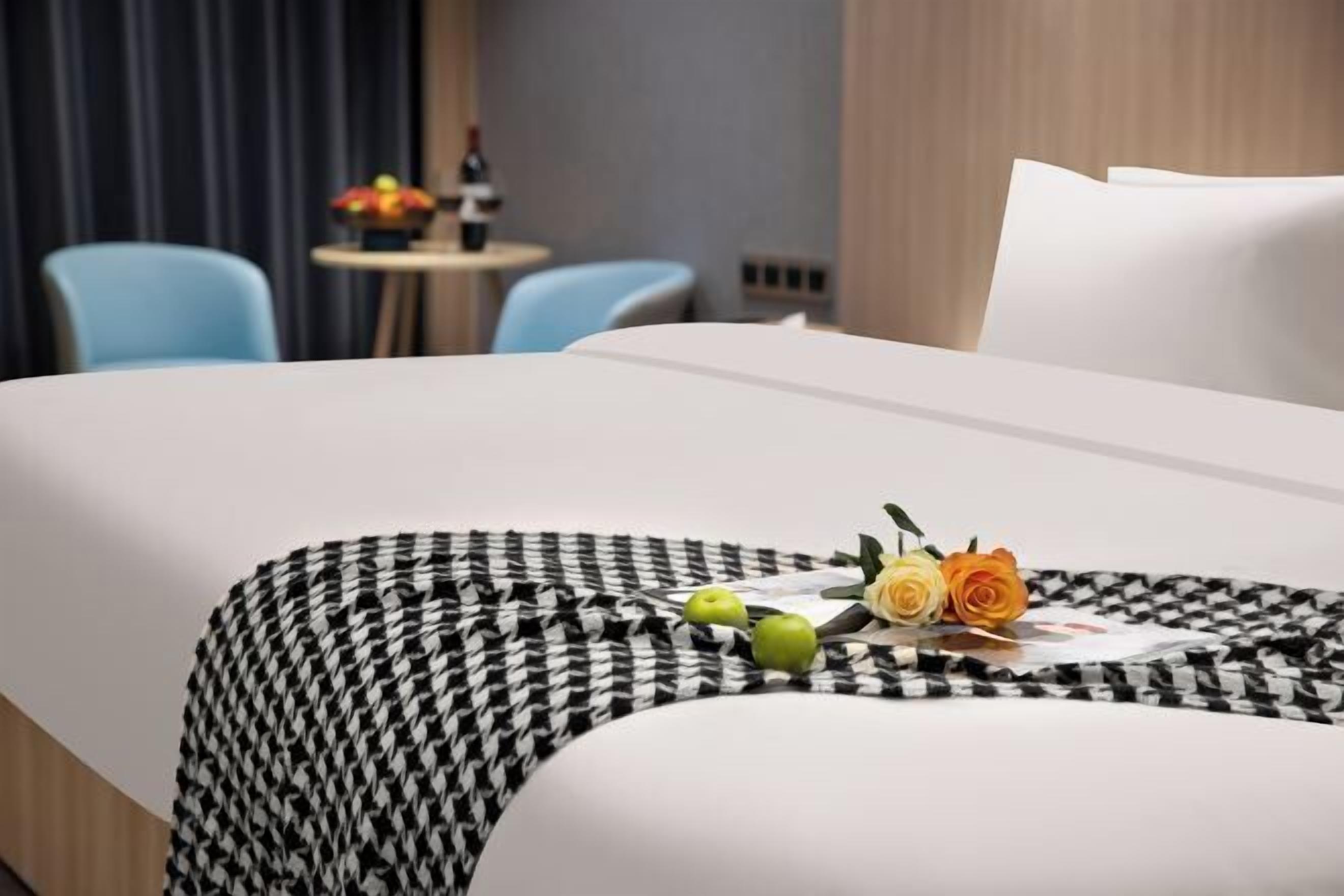 A hotel room with a neatly made bed, a small round table with a vase of flowers, and two blue chairs.