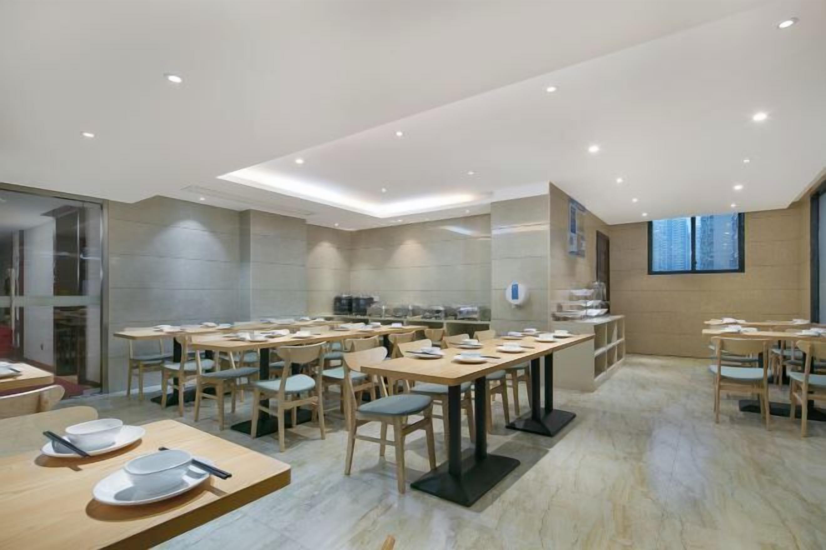 A modern dining area with multiple tables and chairs, recessed ceiling lights, and a large window providing a view of the city.