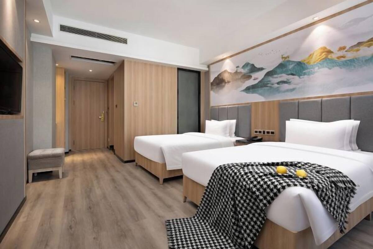 A hotel room with two beds, a houndstooth throw blanket, and a mural on the wall.