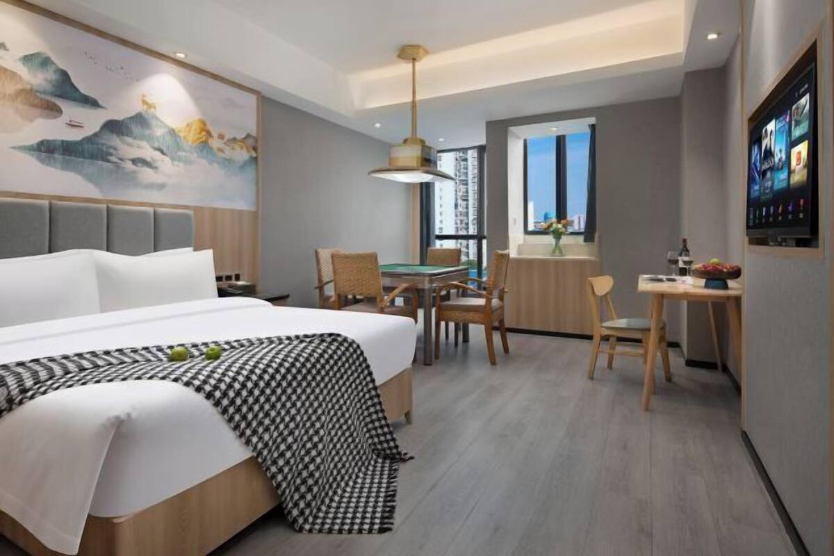 A modern hotel room with a large bed, a dining area, and a TV on the wall.
