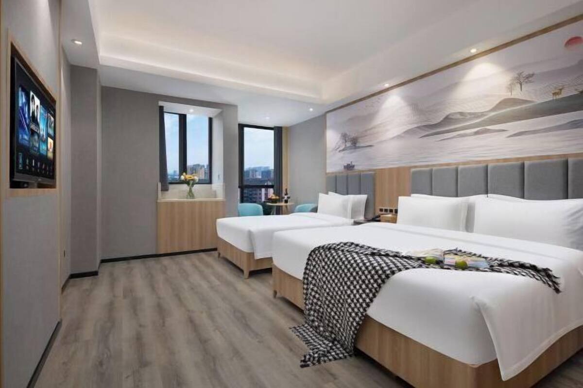 A modern hotel room with two beds, a large window, and a city view.
